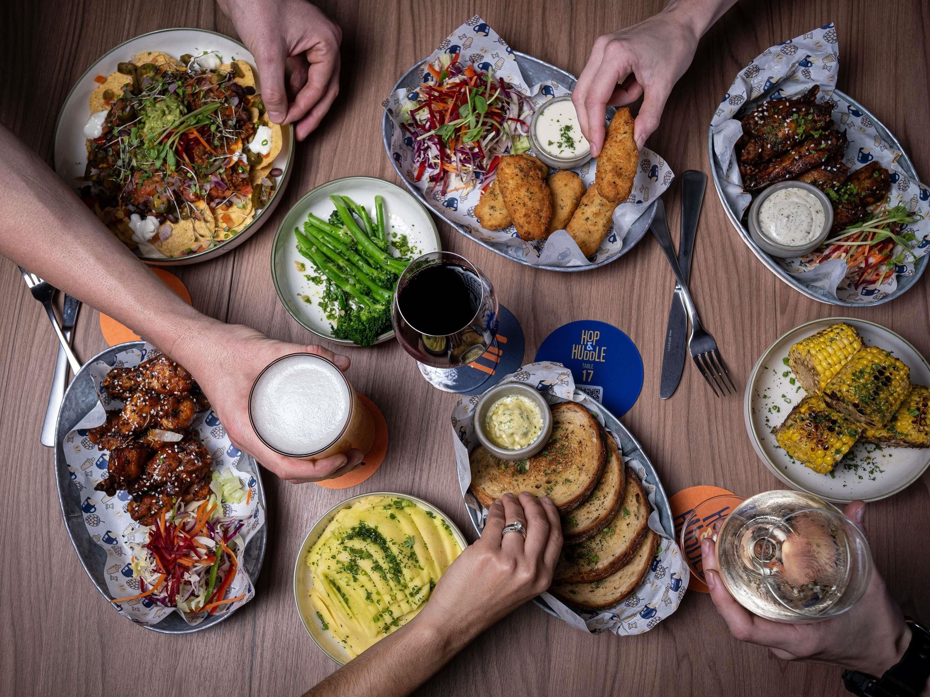 A table with various dishes, including tacos, grilled chicken wings, and corn on the cob, along with drinks and a beer mug.
