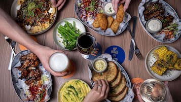 Une table garnie de divers plats, notamment des tacos, des ailes de poulet grillées et des épis de maïs, ainsi que des boissons et une chope de bière.