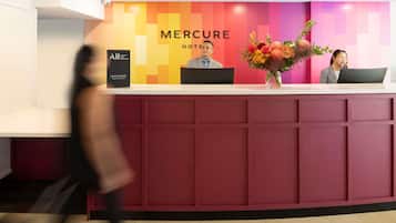Una recepción de hotel con diseño moderno, que destaca un letrero grande de 'Mercure Hotel' y un arreglo floral.