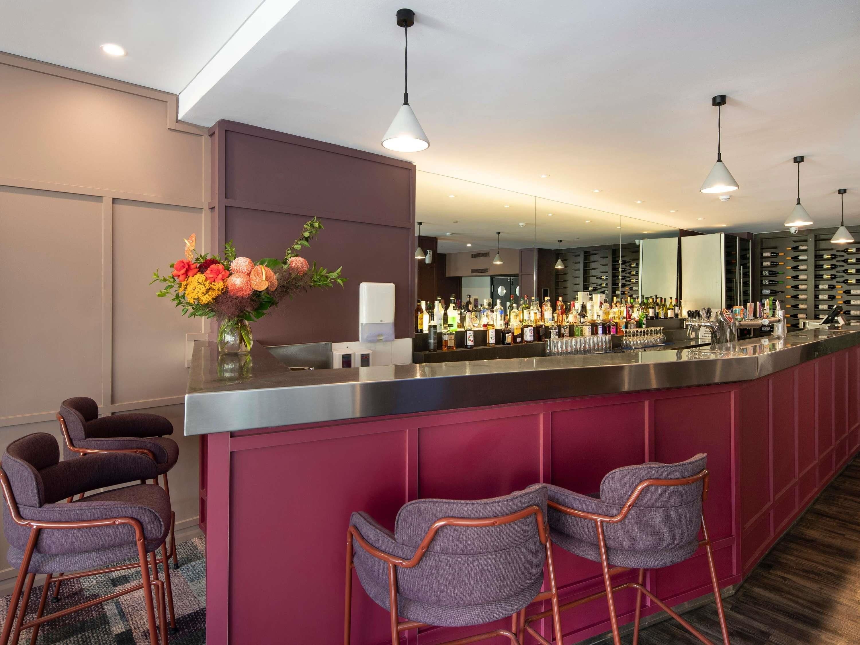 A bar area with a long counter, multiple bottles of alcohol, and bar stools.