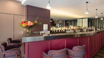 A bar area with a long counter, multiple bottles of alcohol, and bar stools.