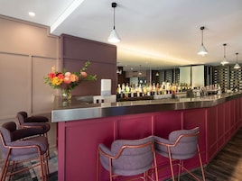 A bar area with a long counter, multiple bottles of alcohol, and bar stools.