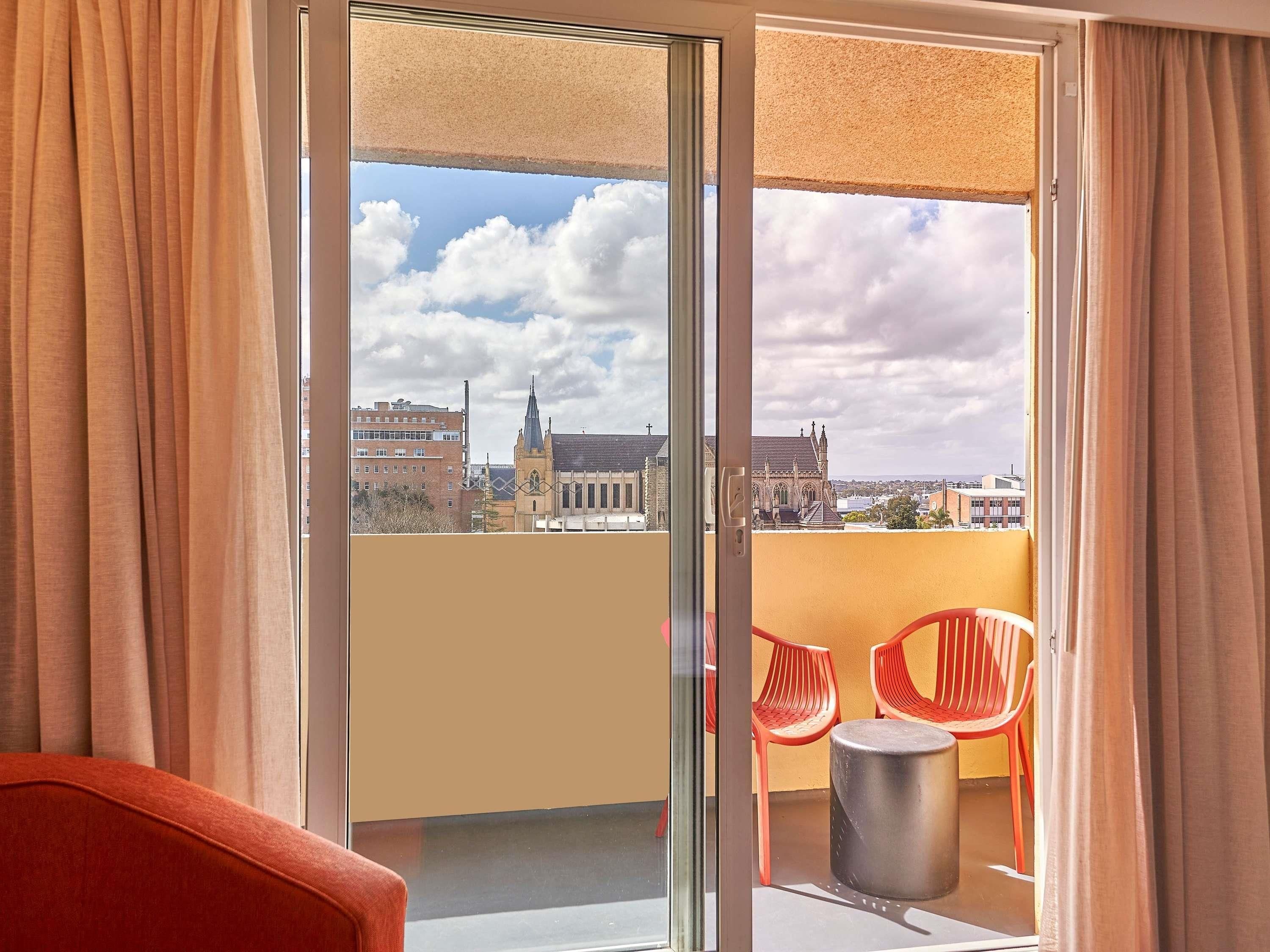 Ein Balkon mit Glastür, roten Plastikstühlen und einem kleinen runden Tisch.