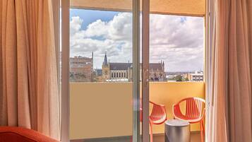 Ein Balkon mit Glastür, roten Plastikstühlen und einem kleinen runden Tisch.