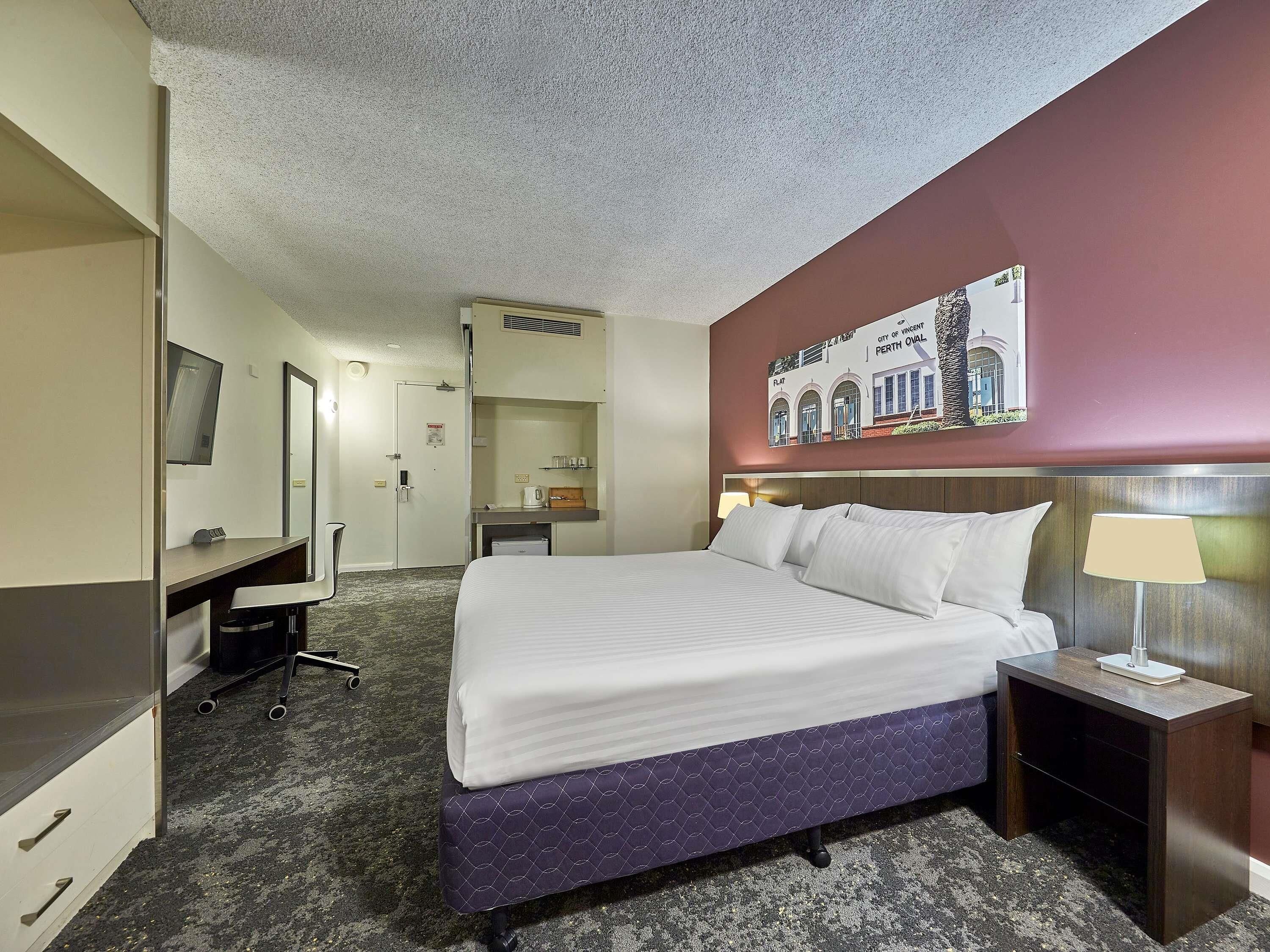 Een hotelkamer met een bed, nachtkastje, bureau, stoel en een spiegel.