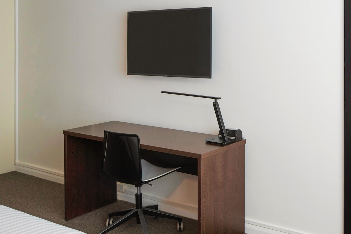 A modern office space with a wooden desk, a black office chair, and a mounted flat-screen TV.