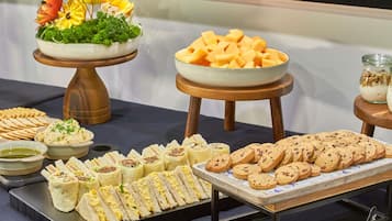Una mesa de buffet con diversos alimentos, incluyendo sándwiches, galletas y un centro de mesa decorativo.