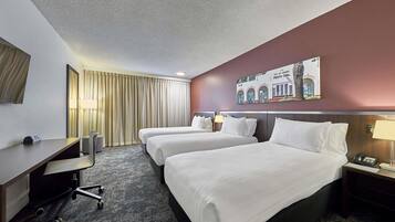 A hotel room with two beds, a desk, a chair, a lamp, and a painting on the wall.