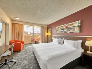 Habitación de hotel con una cama grande, un escritorio, una silla y vista a un paisaje urbano a través de la ventana.