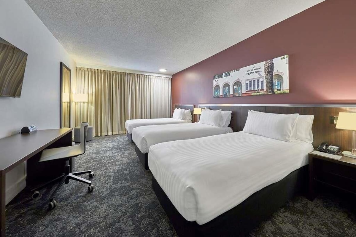 A hotel room with two beds, a desk, a chair, a lamp, and a wall-mounted artwork.