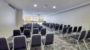A conference room with rows of chairs, a projector, and a large window with a view of trees. - Mercure Perth On Hay (Perth)