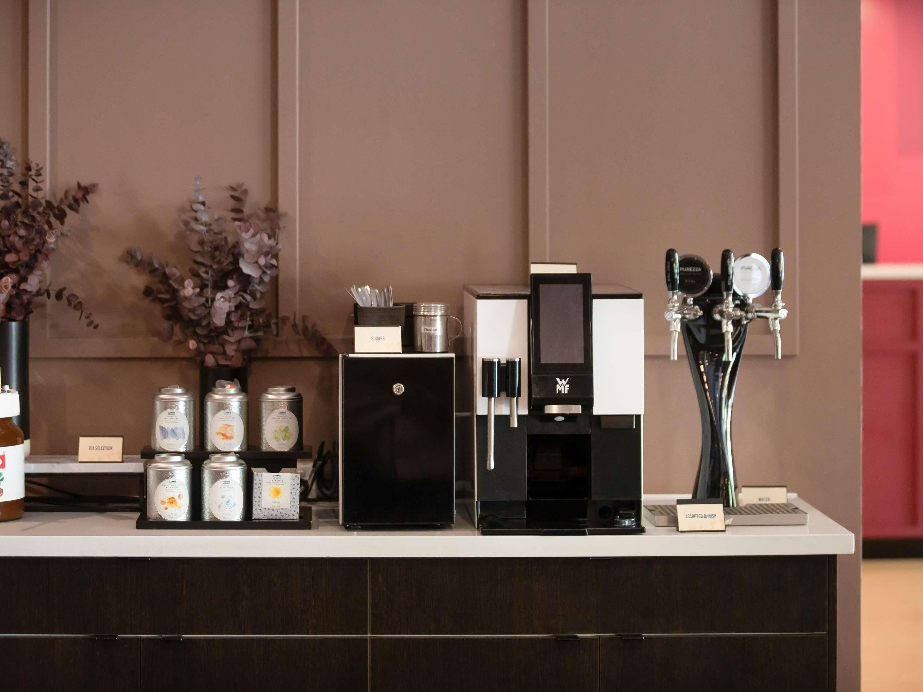 A coffee station with a coffee machine, sugar and milk dispensers, and tea selection.