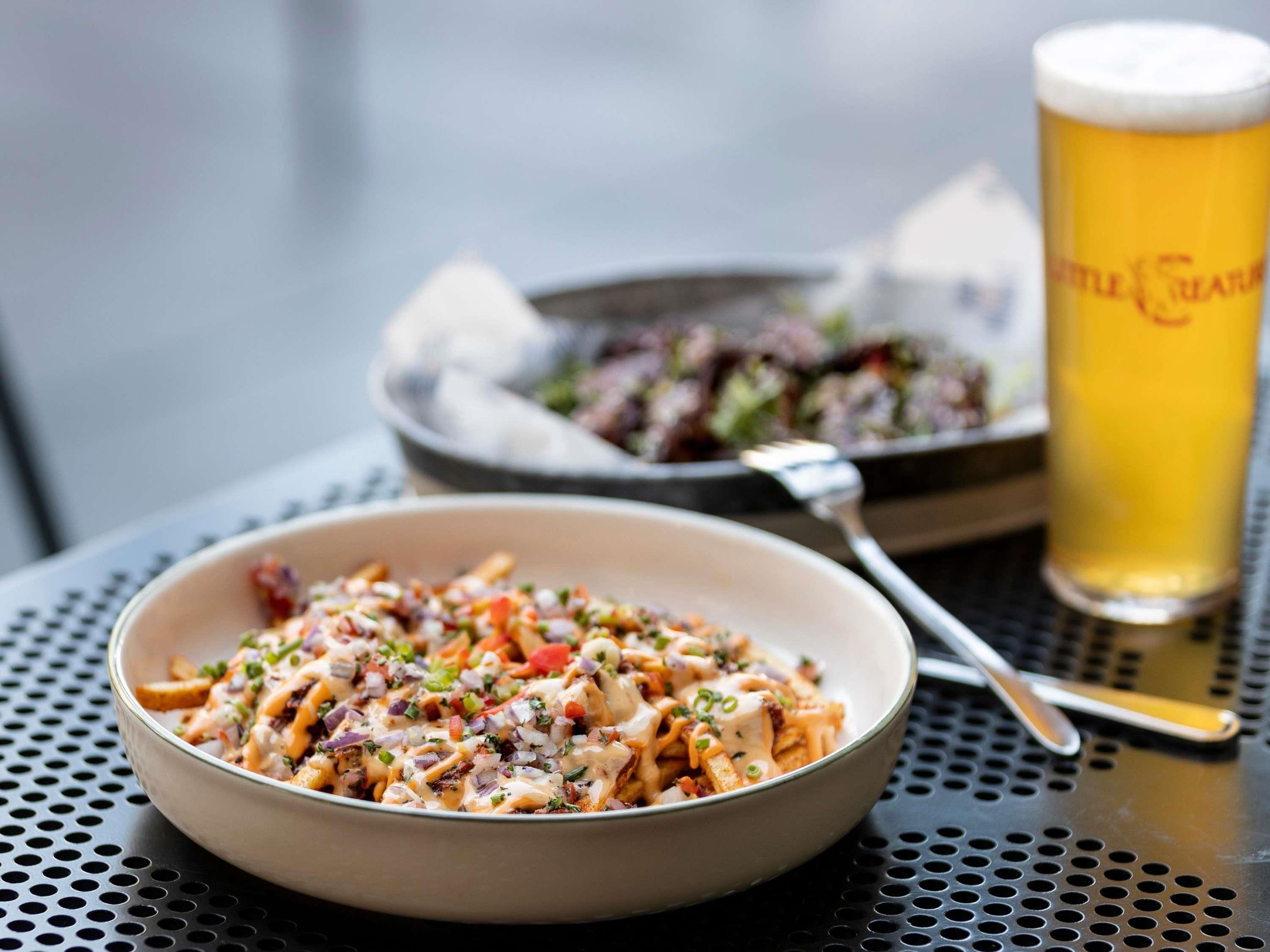 A bowl of pasta with a creamy sauce, a glass of beer, and a plate of salad on a table.