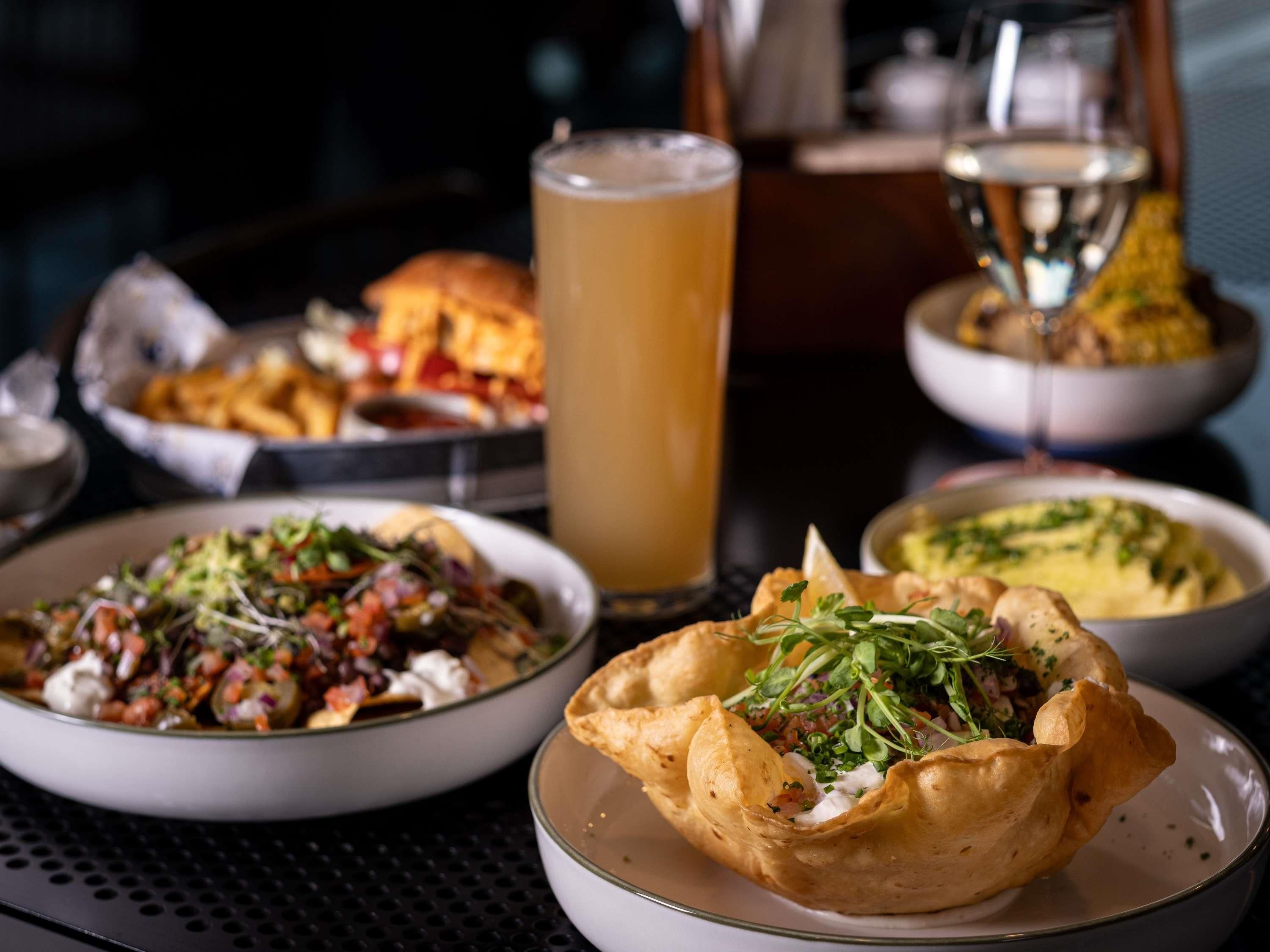 A dining table with various dishes, a glass of beer, and a glass of white wine.