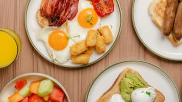 A breakfast setting with plates of eggs, bacon, tomatoes, beans, and toast.
