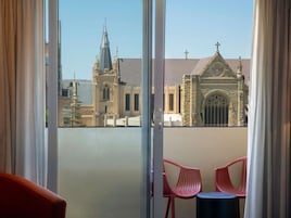 A balcony with two red chairs and a small table, overlooking a church and a building with a pointed roof.