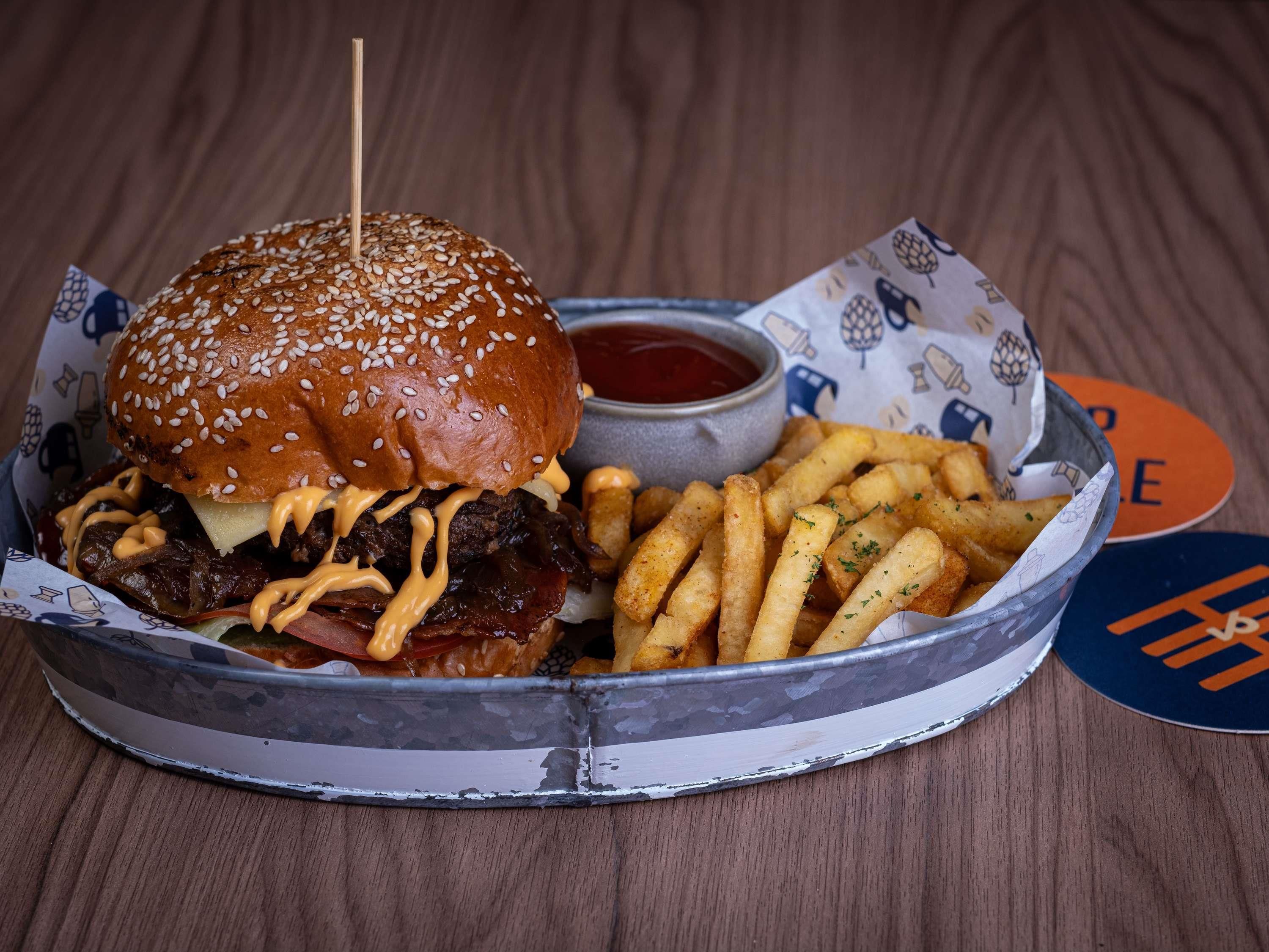 A burger with sesame seeds on the bun, a side of fries, and a small container of ketchup.