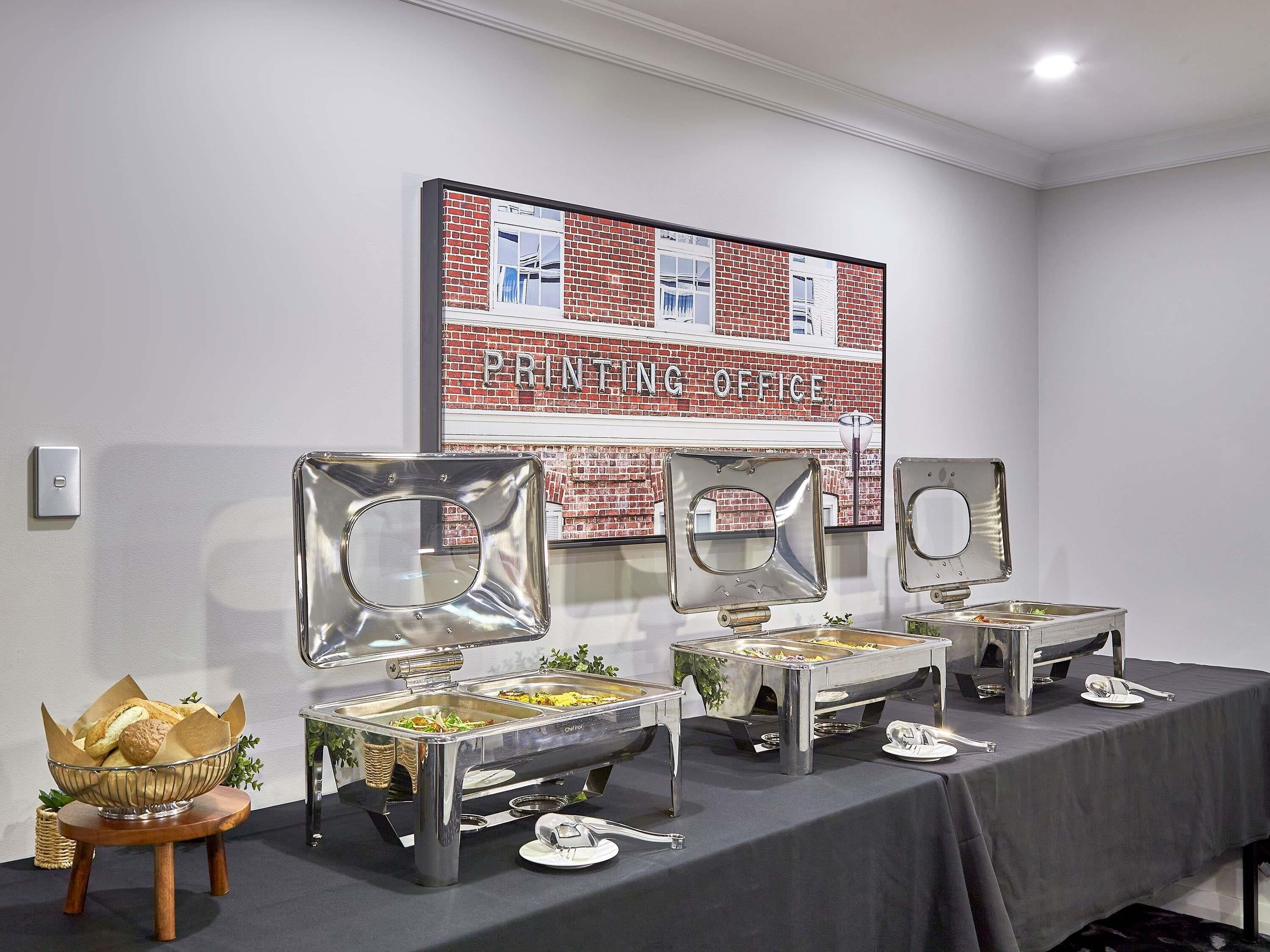 A buffet setup with multiple serving stations, a framed sign reading "Printing Office," and a small decorative plant.