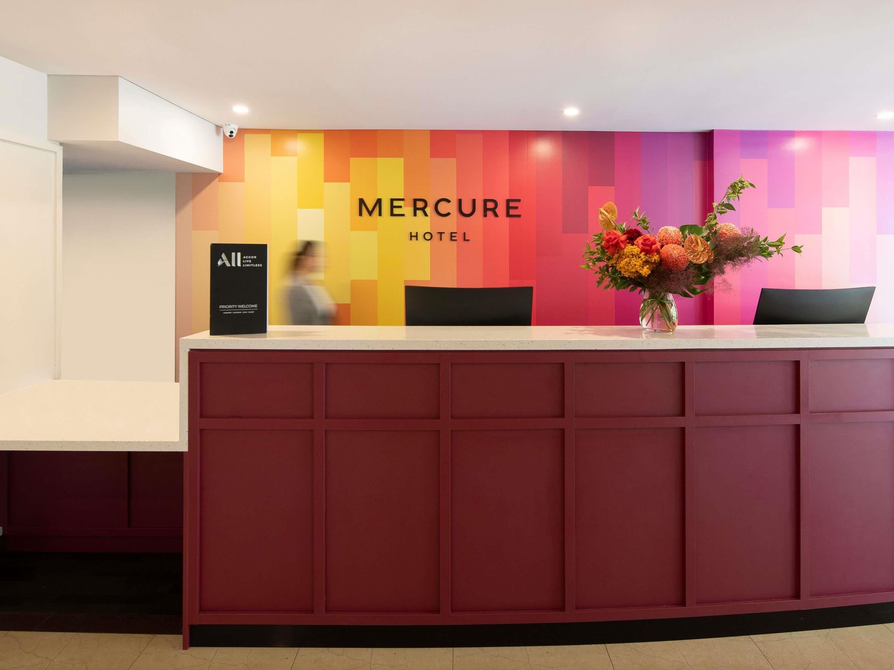 Een receptiebalie met een bordje 'Mercure Hotel', een bordje 'Priority Welcome' en een bloemstuk.