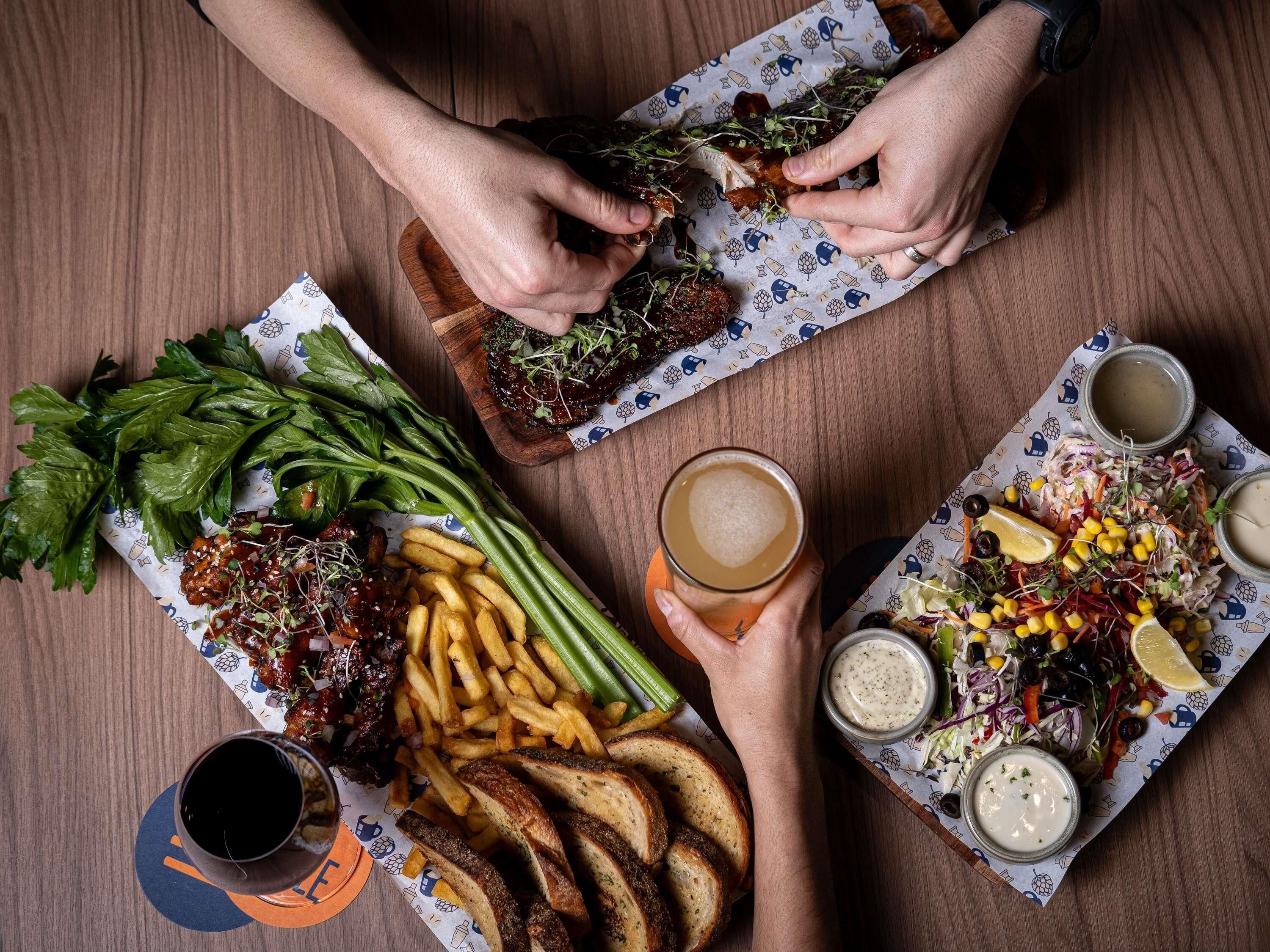 Uma mesa com diversos alimentos, incluindo batatas fritas, salada e pão, além de bebidas e acompanhamentos.