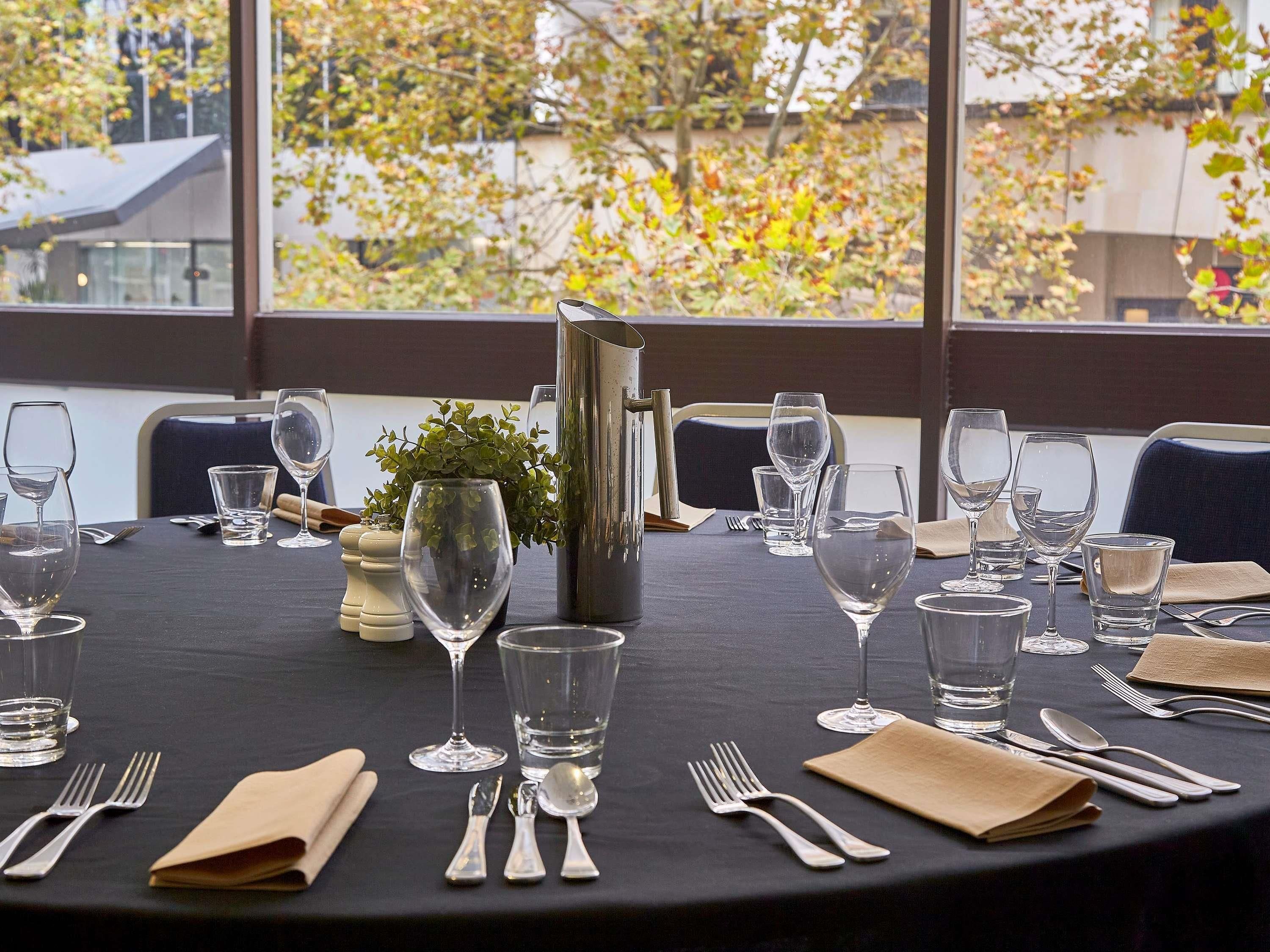 A table set for dining with wine glasses, water glasses, and cutlery, a salt and pepper shaker, and a small plant centerpiece.