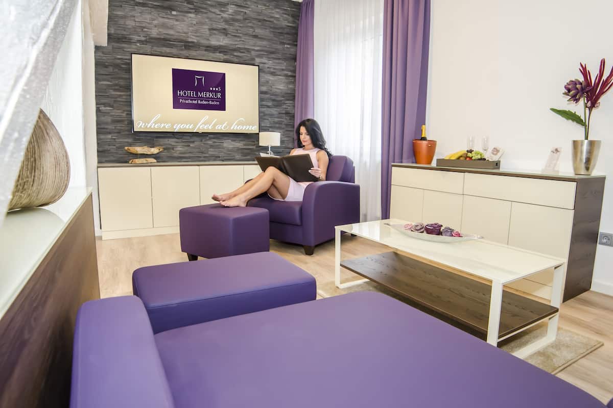 Una habitación de hotel moderna con un sofá morado, una mesa de centro de madera y un televisor de pantalla plana montado en una pared de piedra.