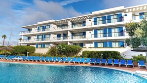 Un hôtel avec une piscine, des chaises bleues et un ciel dégagé.