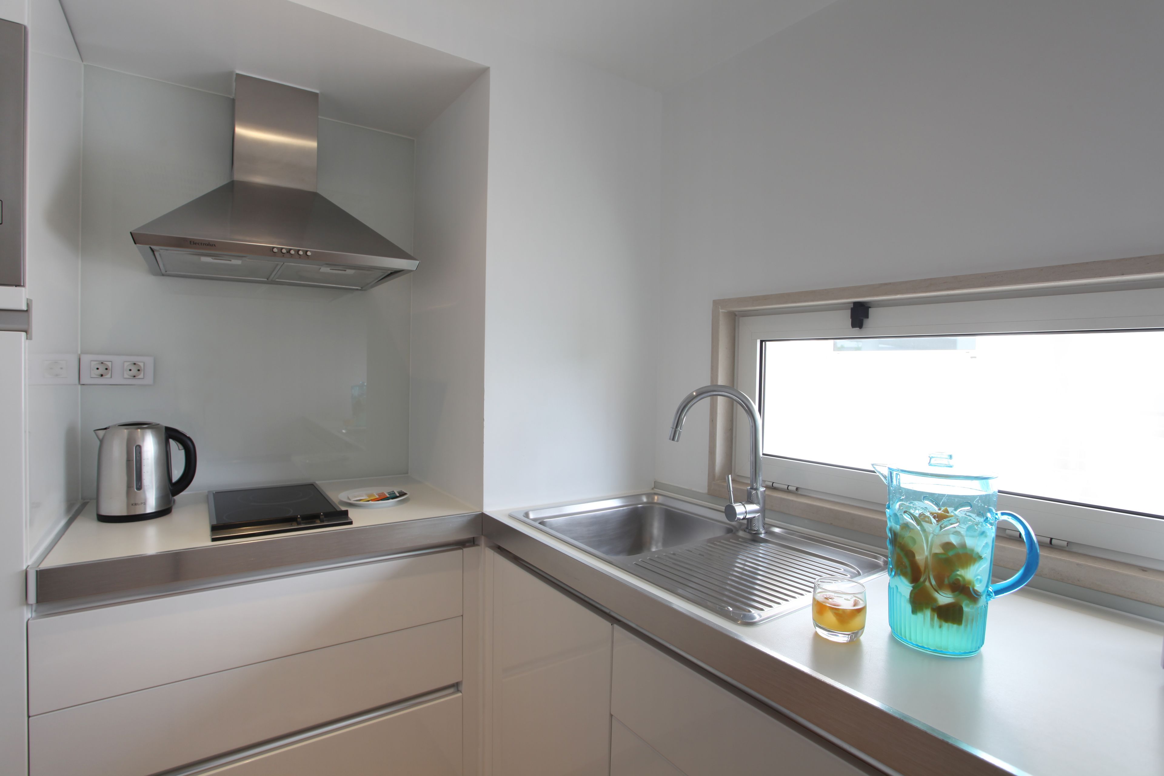 A modern kitchen with a stainless steel sink, a kettle, and a pitcher on the counter.