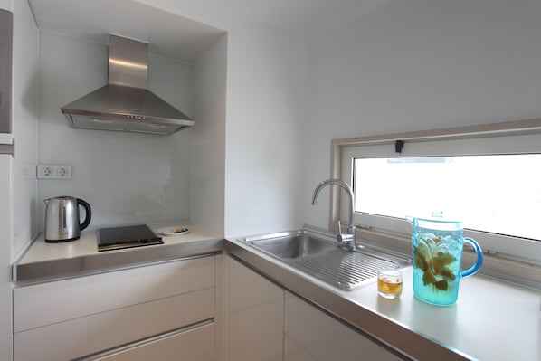 Una cocina moderna con un lavamanos de acero inoxidable, una tetera y una jarra en la encimera.