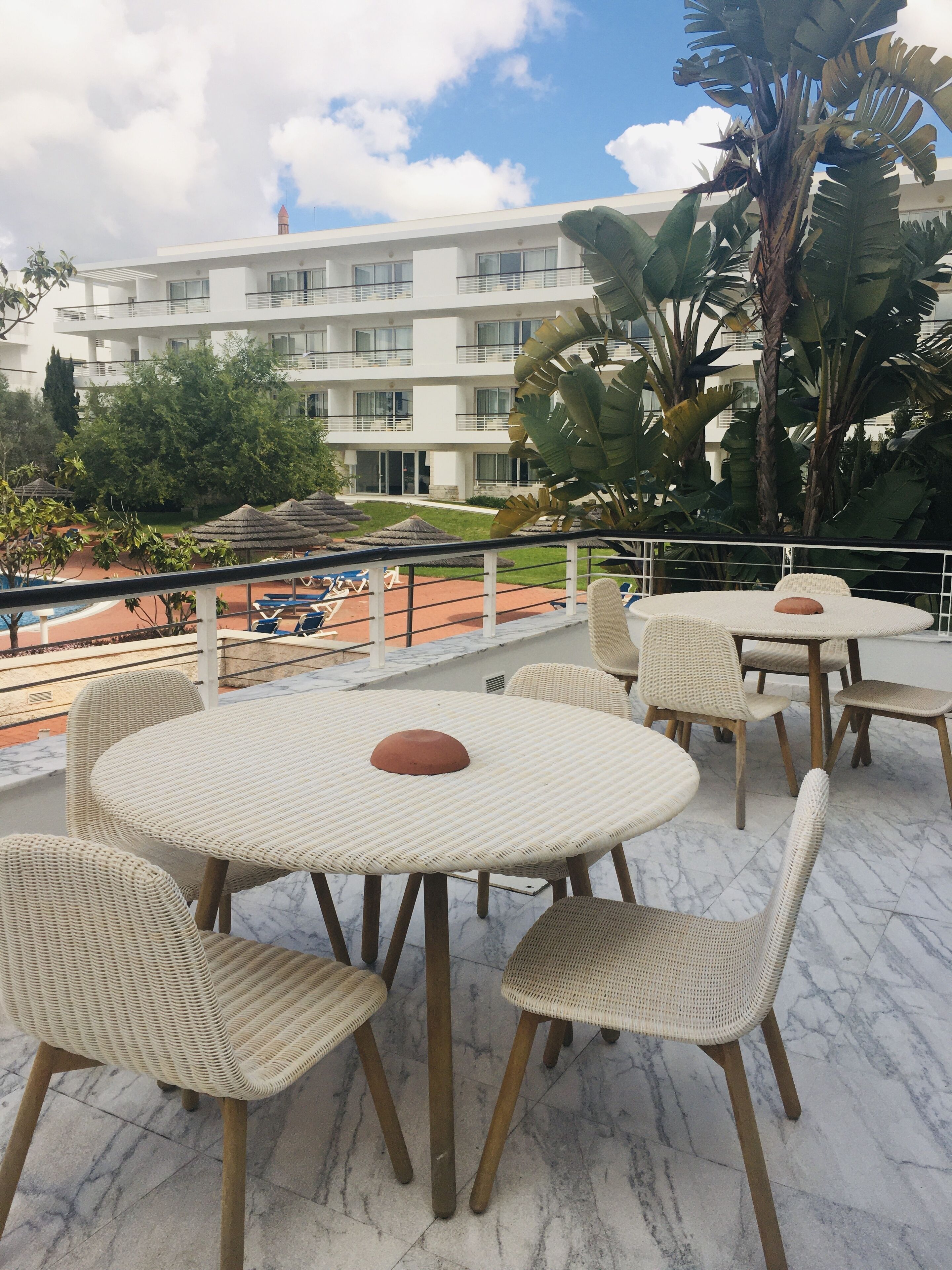 Une terrasse sur le toit, avec des tables rondes et des chaises en osier, d’où l’on peut admirer un immeuble doté de balcons et une vue imprenable sur le ciel.