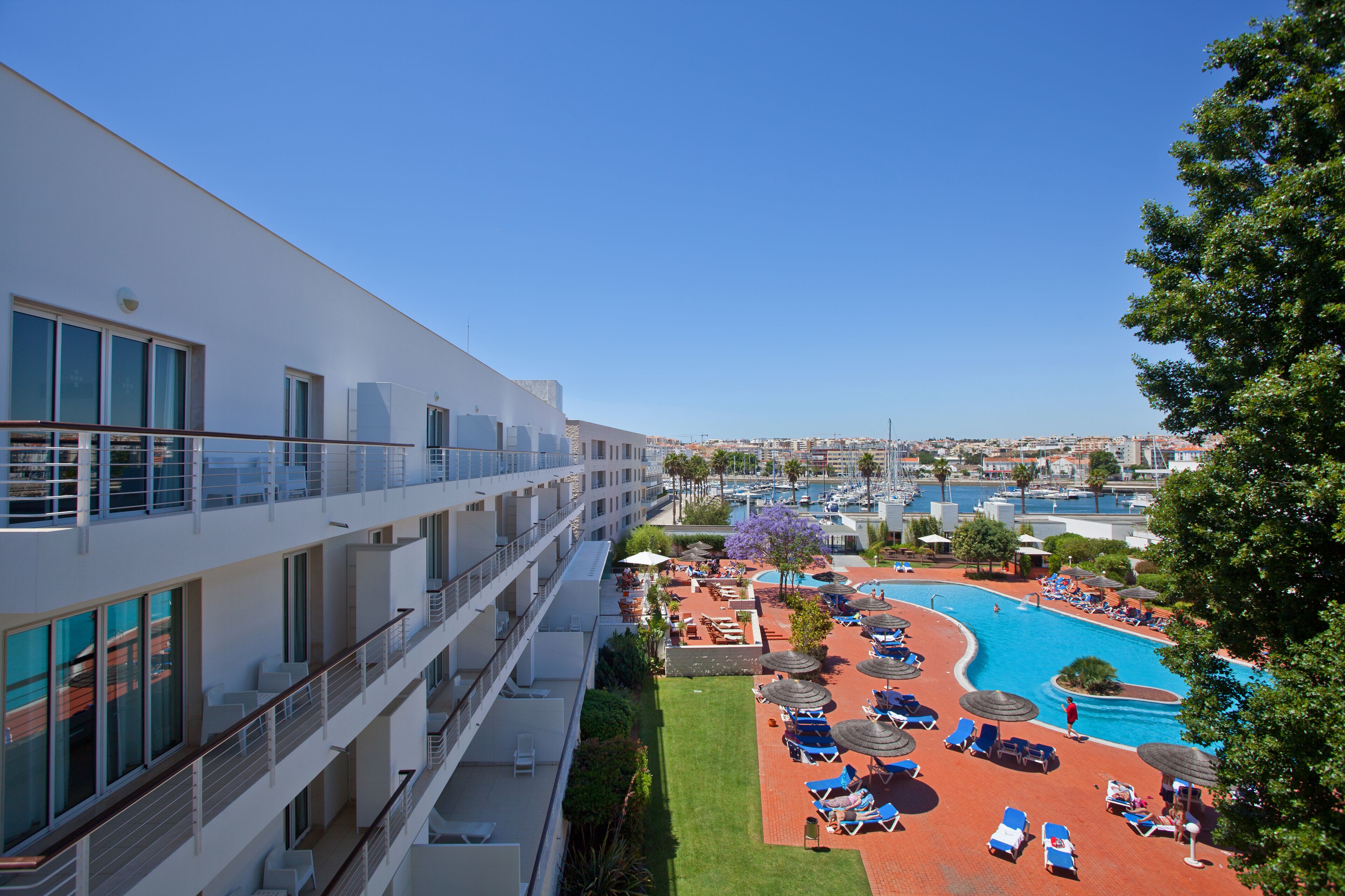 Un hotel con piscina en la azotea, varios balcones y vistas a la ciudad.