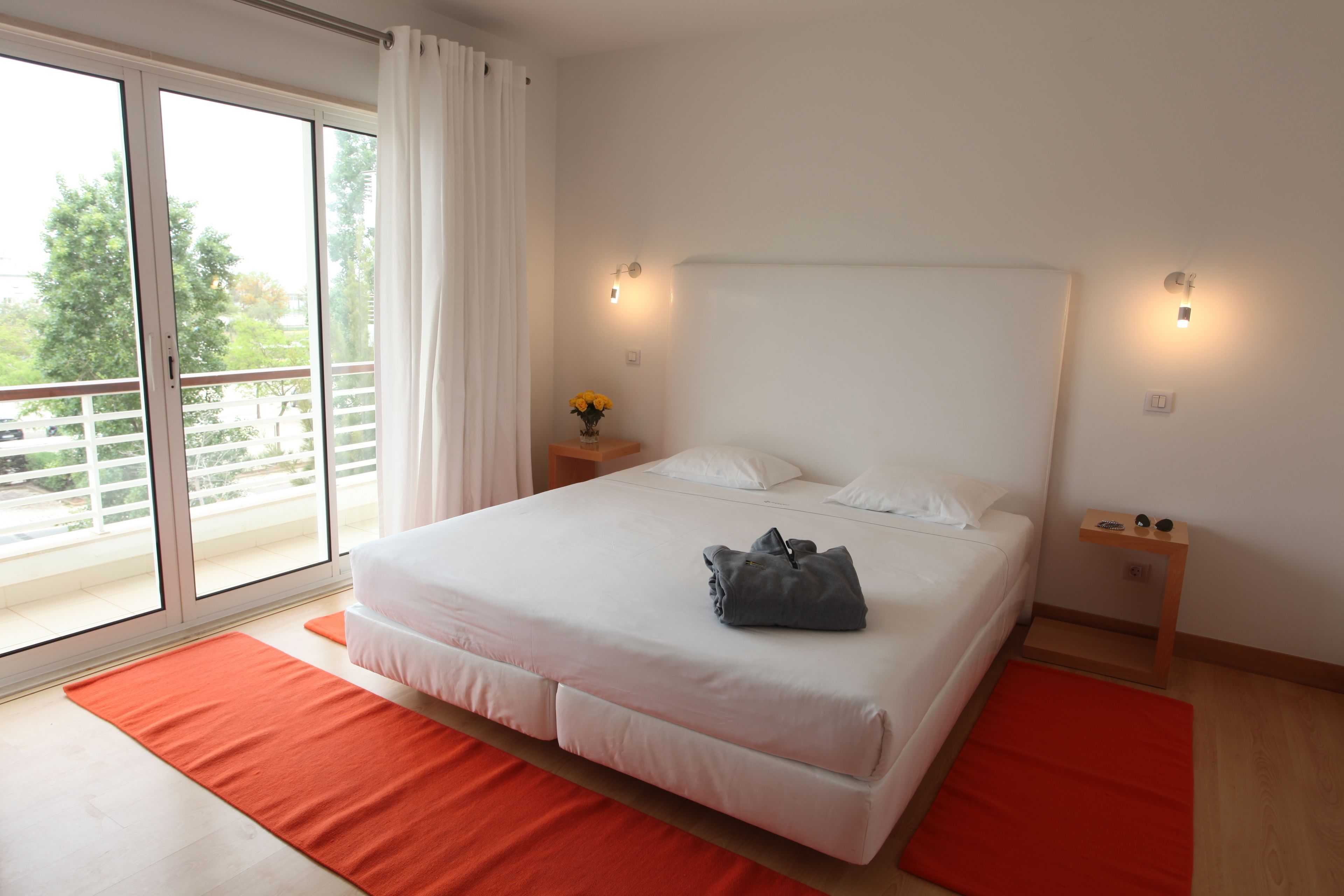 Een slaapkamer met een groot bed, twee nachtkastjes, een raam met gordijnen en uitzicht op groen buiten.