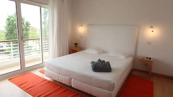 Un dormitorio con una cama grande, dos mesitas de noche, una mesilla auxiliar, una ventana con cortinas y vistas a zonas verdes.