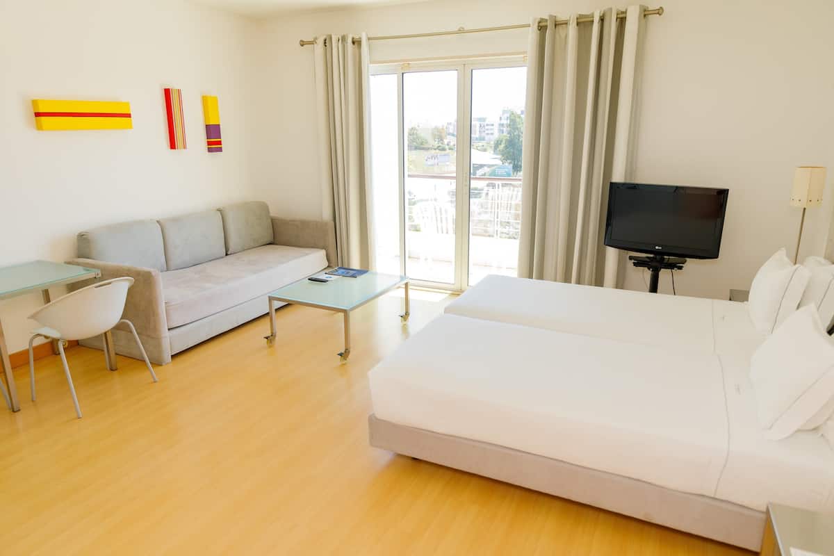 Ein modernes Hotelzimmer mit einer Couch, einem Bett, einem Fernseher und einem Tisch.