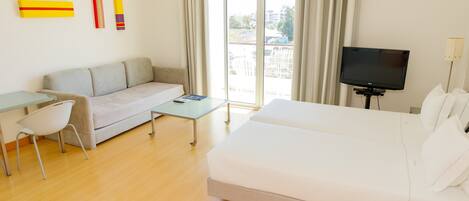 A modern hotel room with a sofa, a bed, a TV, and a table.