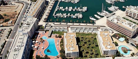 A marina with numerous boats docked, a swimming pool, and a hotel building with multiple balconies.