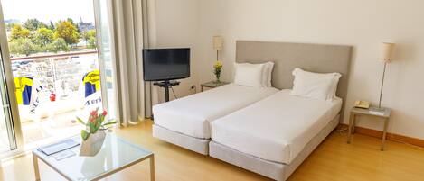 A hotel room with a bed, a TV, a bedside table, a lamp, and a view of the outside.