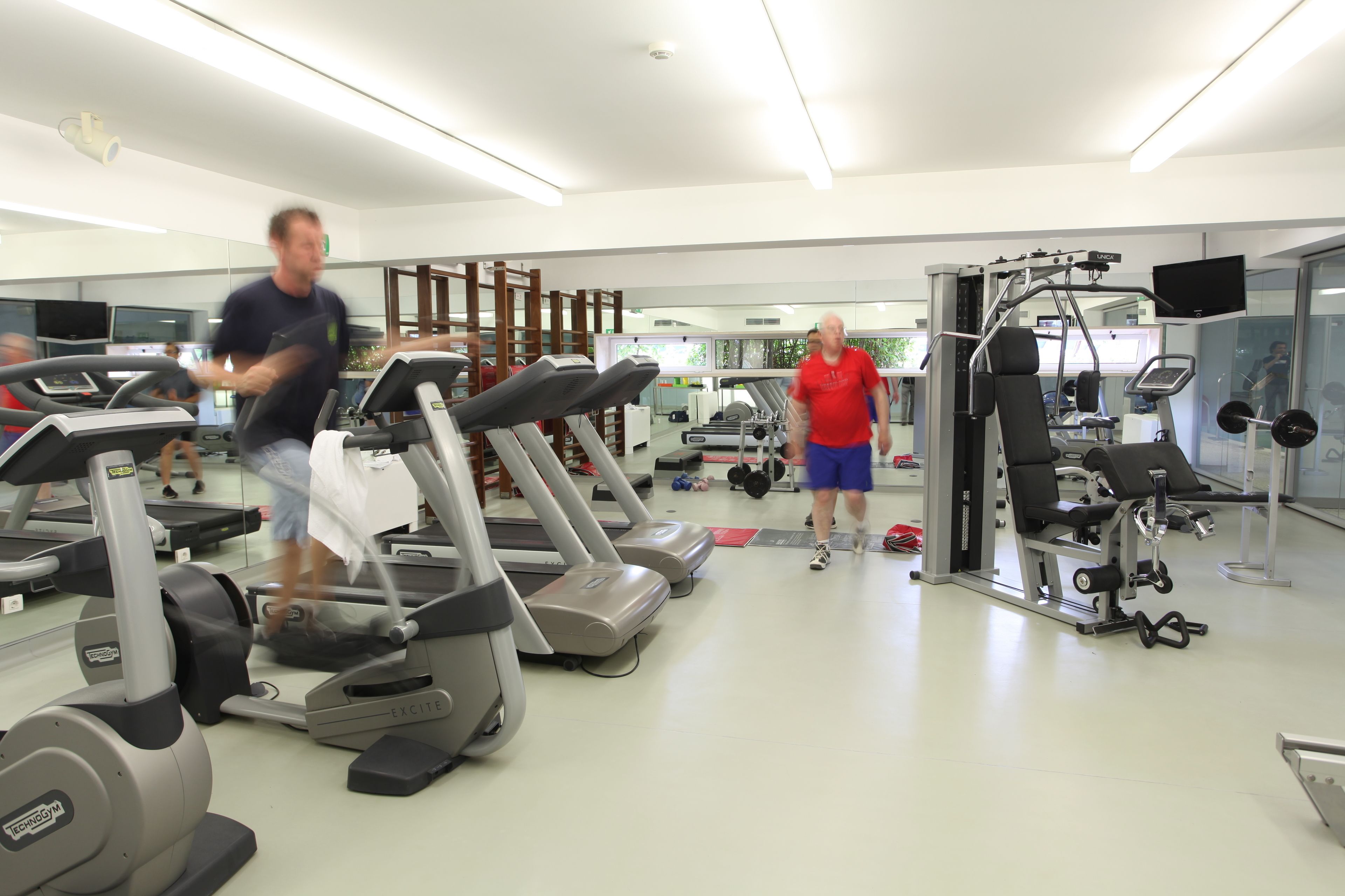 Une salle de sport équipée de tapis de course, d’appareils de musculation et d’un mur recouvert de miroirs.