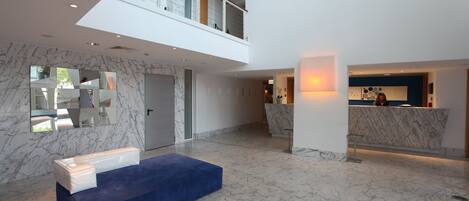 A modern lobby with a marble floor, a reception desk, and a blue seating area.