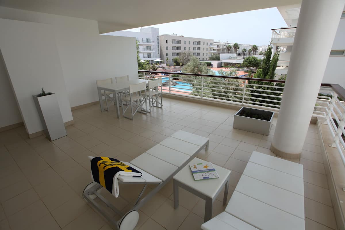 Ein Balkon mit weißer Möbel, ein Pool und Blick auf umliegende Gebäude.