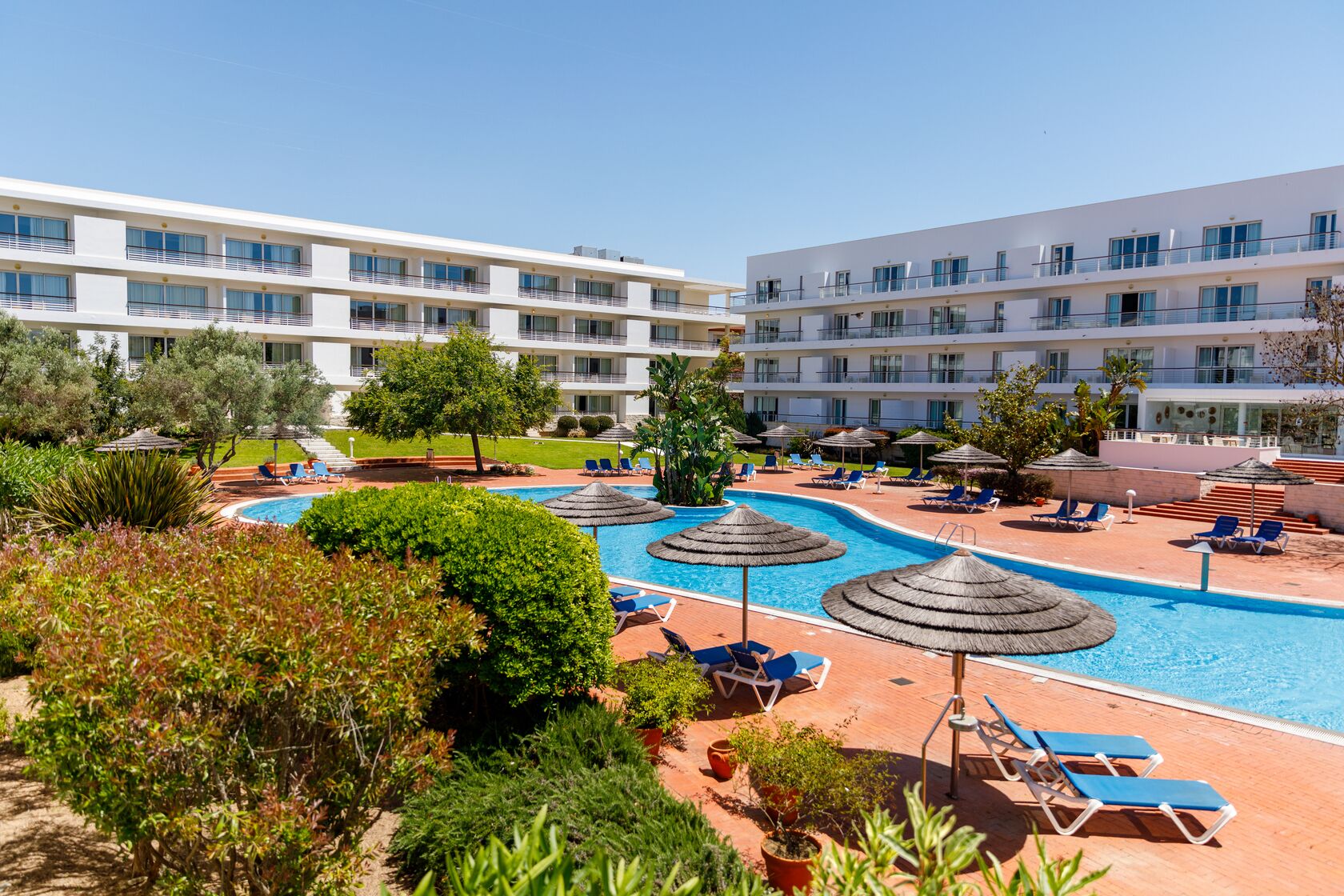 A hotel with a swimming pool, sun loungers, and a well-maintained garden.