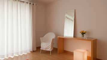 Una habitación con un escritorio de madera, una silla blanca, un espejo y un jarrón con flores.