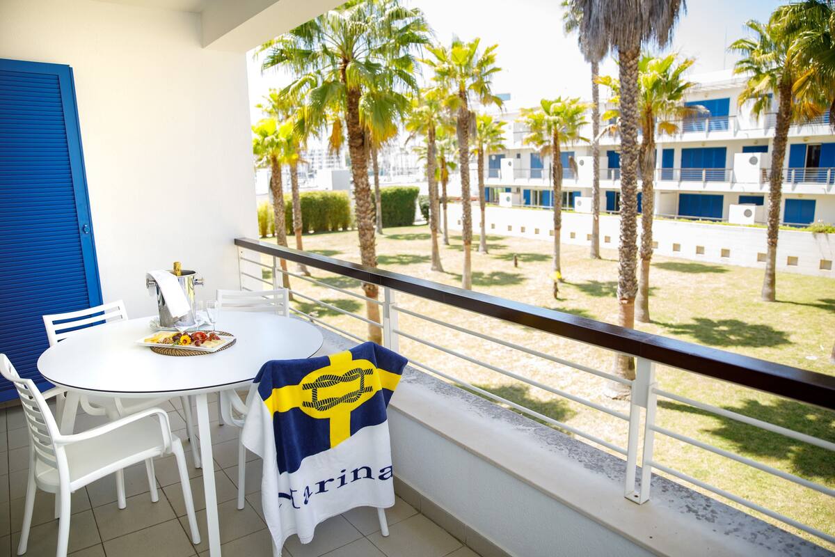 Ein Balkon mit einem weißen Tisch, Stühlen und einer Tischdecke mit gelb-blauen Mustern.