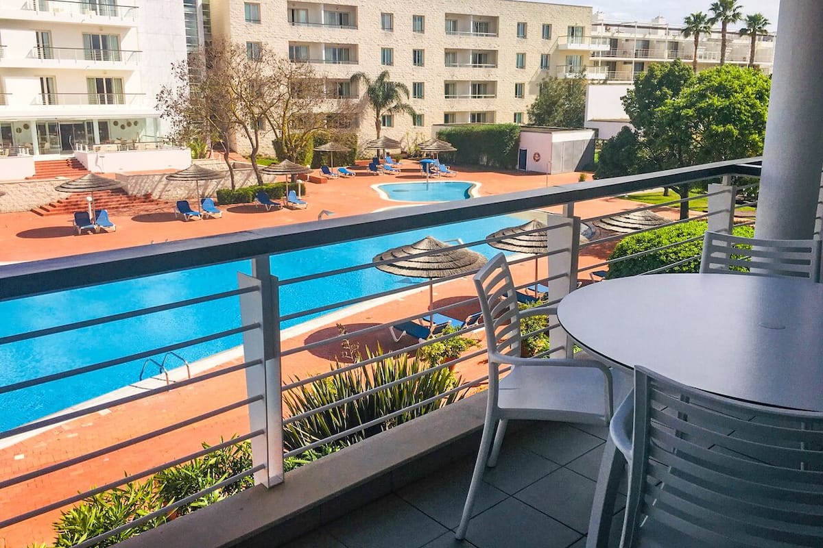 Ein Balkon mit Blick auf einen Swimmingpool, Liegestühlen und einem Tisch.