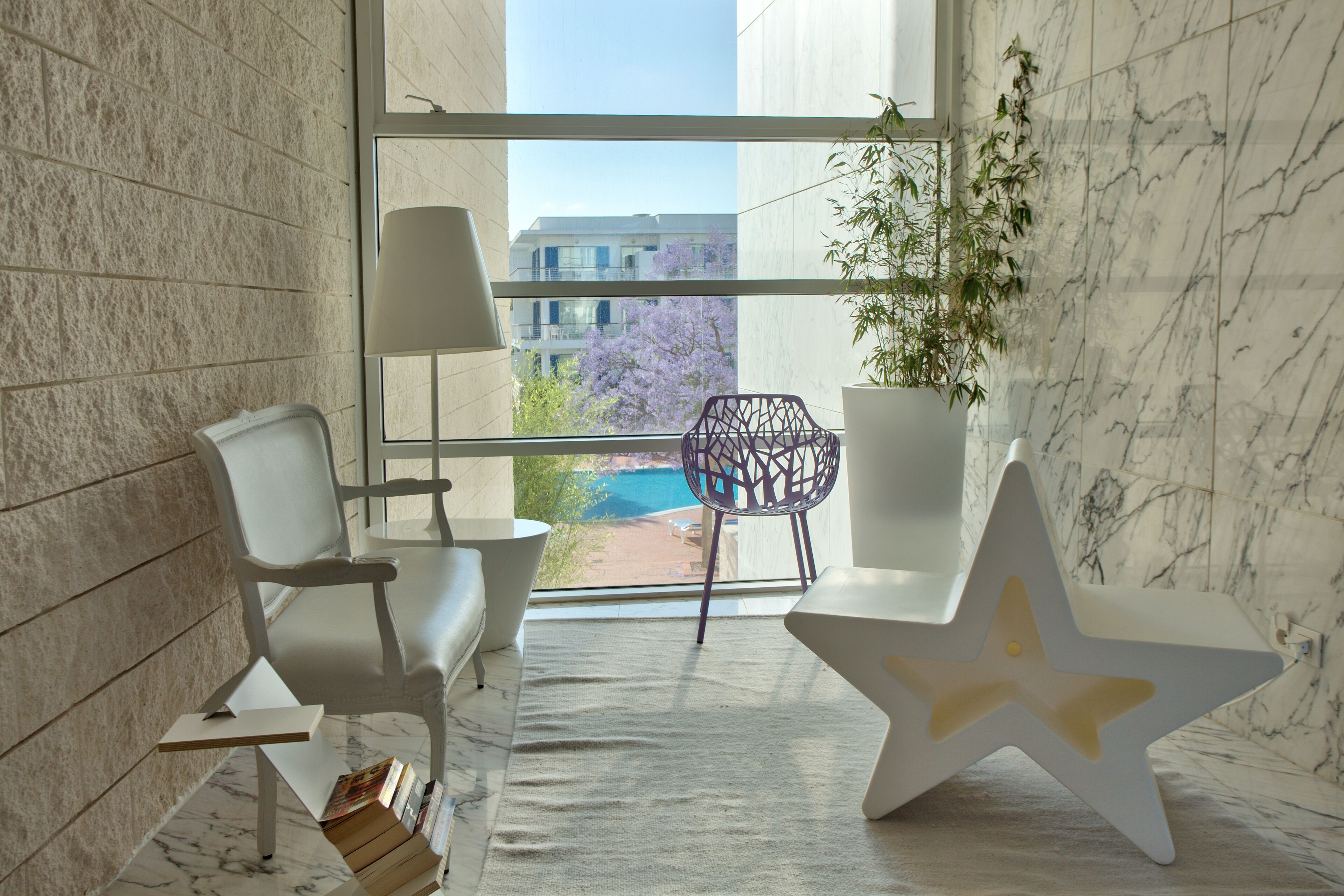 Un área de espera moderna con un amplio ventanal, una mesa con forma de estrella y una planta en maceta.