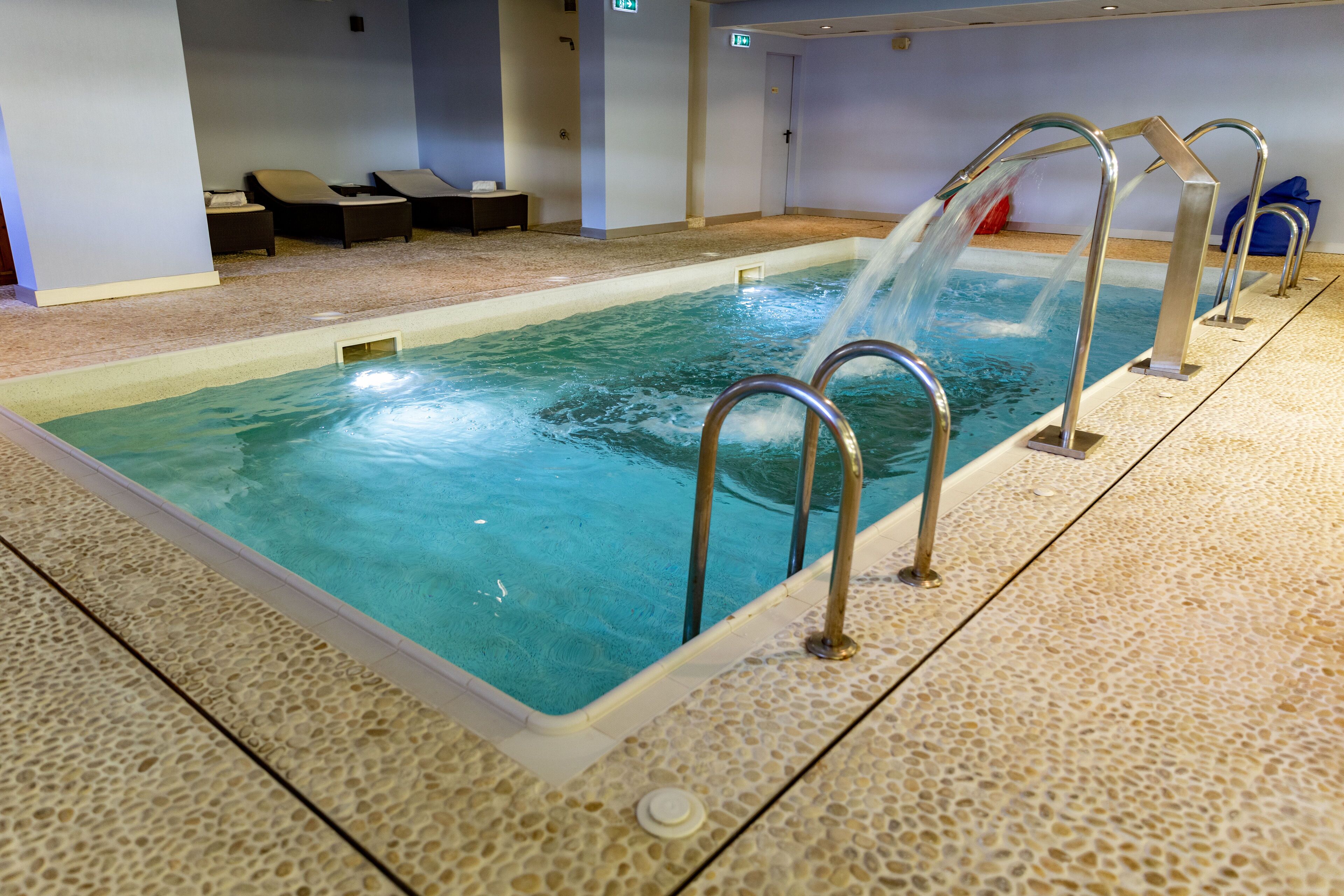 An indoor swimming pool with a water slide, lounge chairs, and a tiled floor.