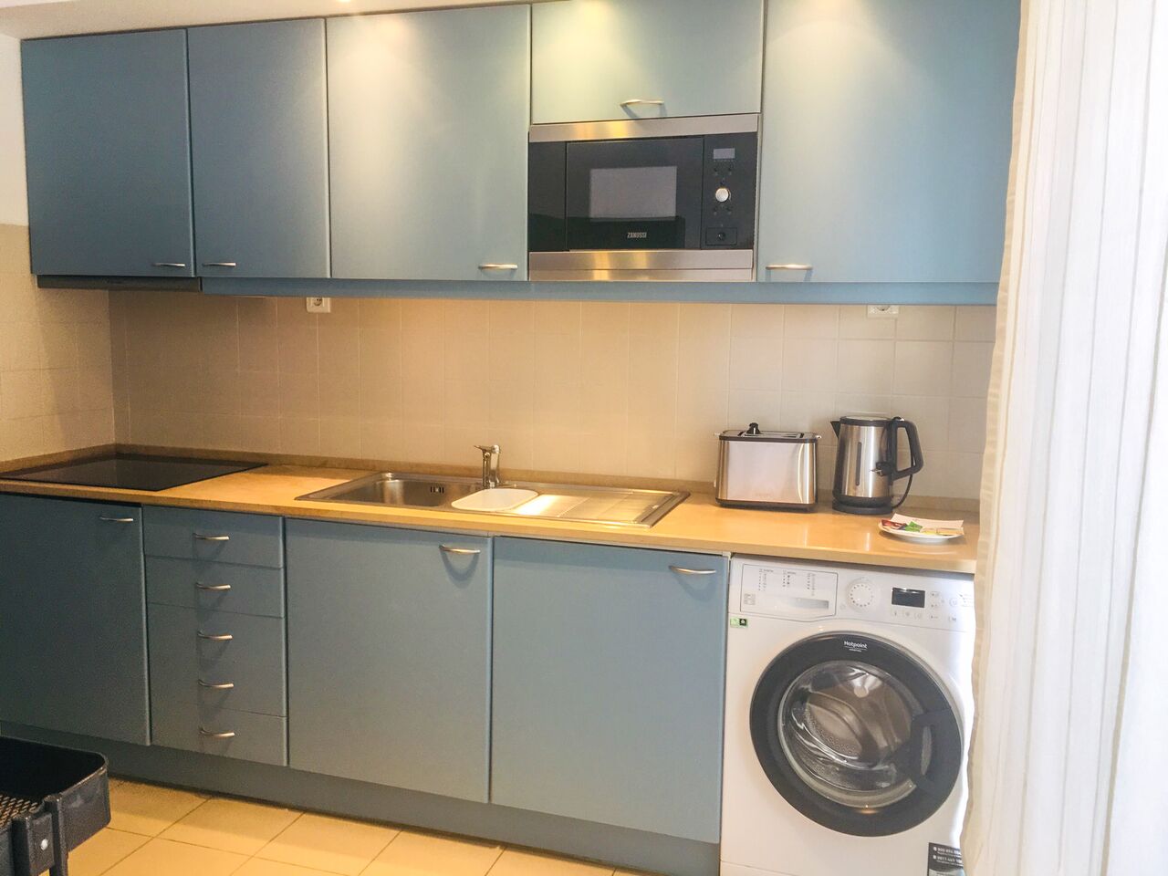 A compact kitchen with a microwave, sink, toaster, and washing machine.