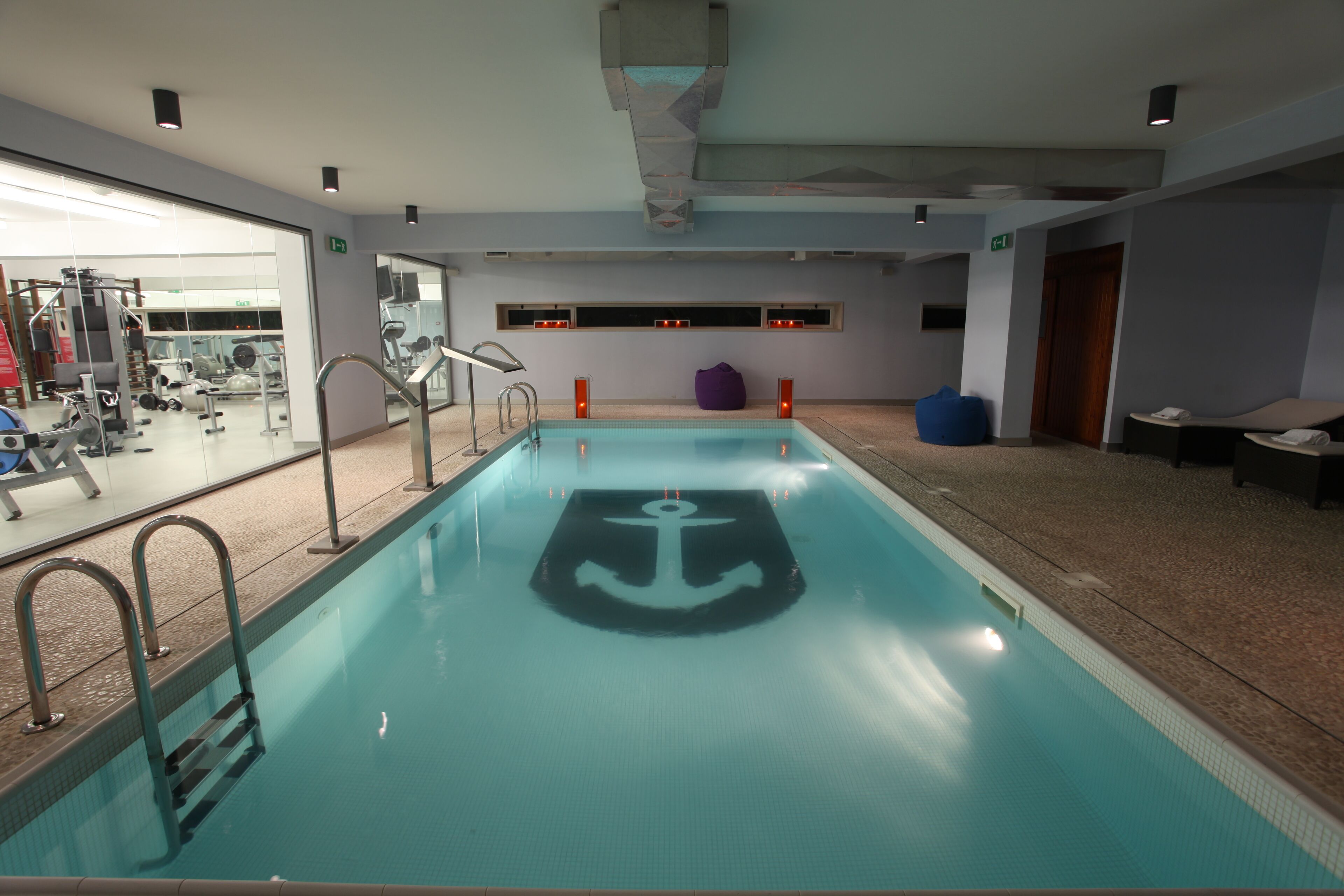 An indoor swimming pool with a central anchor design, surrounded by exercise equipment and seating areas.