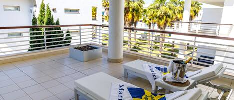 Una terraza en la azotea con sillones de descanso, una mesa con una bebida y vistas a palmeras y un edificio.