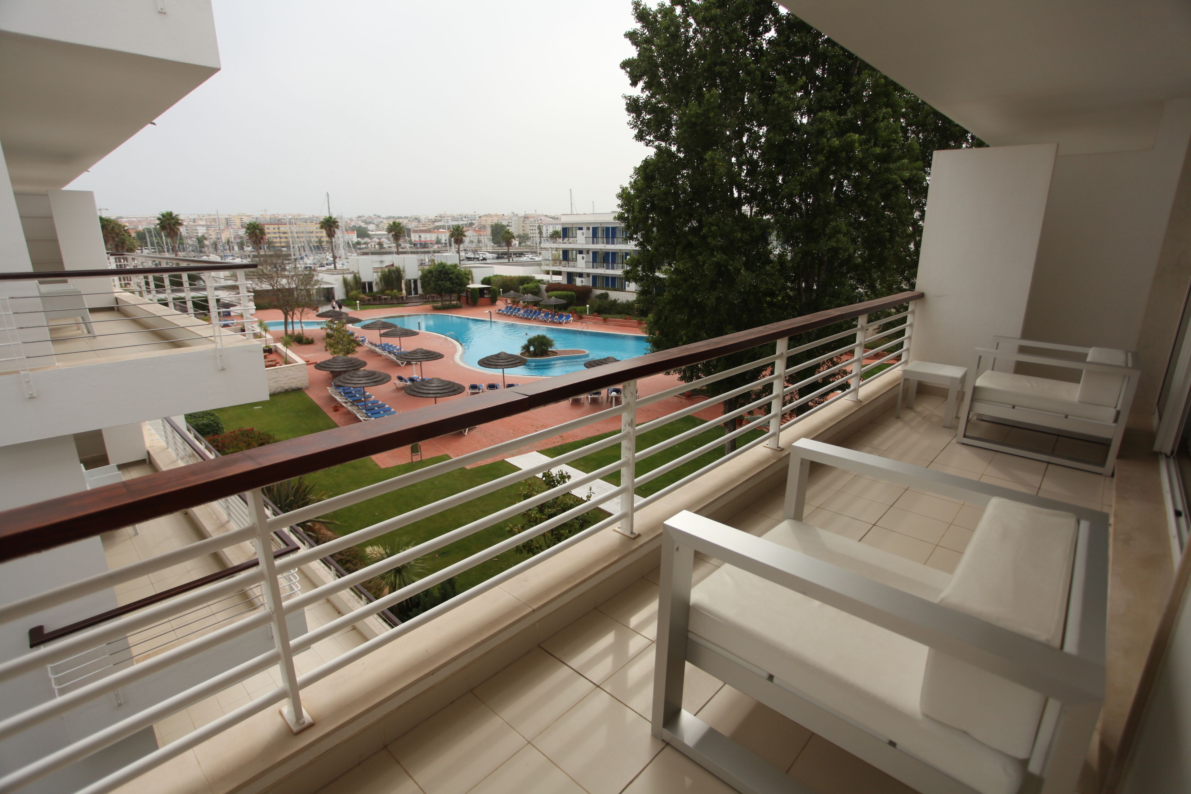 Un balcon avec vue sur une piscine, des chaises longues et un paysage urbain en arrière-plan.